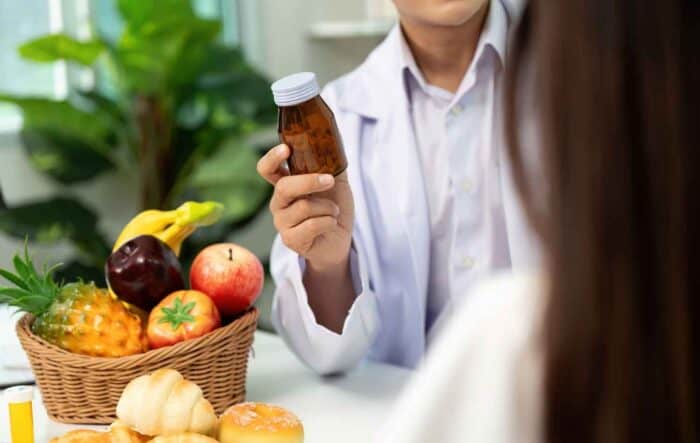 a person holding a supplement bottle containing extracts of various healthy fruits displayed on a table, representing how growing supplement use influences people’s perception of their personal health.