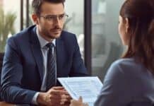How to Build Effective Marketing Strategy Based on Differentiation? A man in a suit and glasses listens intently to a woman holding documents during a meeting in a modern office, conveying a focused and professional tone.