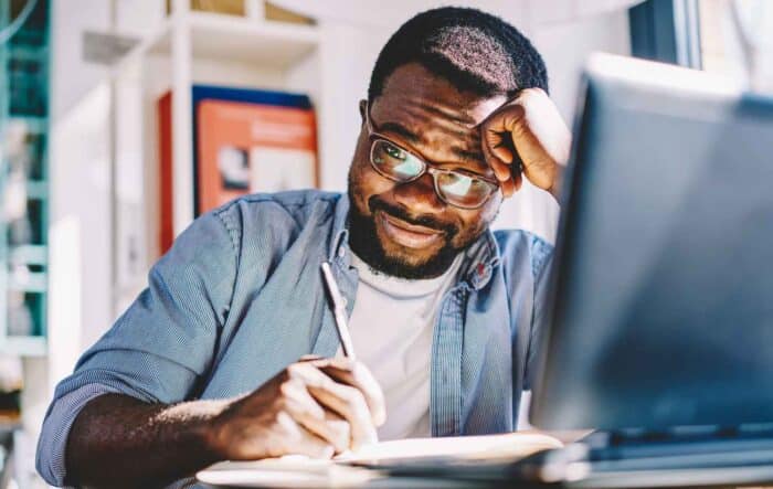 a focused man studying and taking notes at his desk while looking at a laptop, representing choosing the right coaching training program and comparing professional accreditations such as ICF, EMCC, and AC