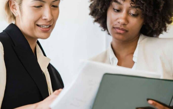 Two professionals in formal attire review documents together. One smiles, suggesting a collaborative and focused work atmosphere.
