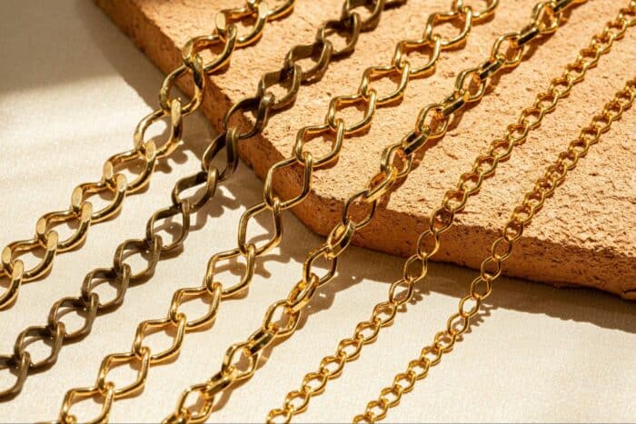 Golden chains of varying link styles rest on a textured surface, illuminated by warm sunlight, creating a luxurious and elegant atmosphere.