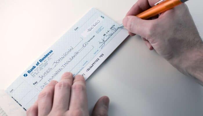 A person writes on a check from "Bank of Business" with an orange pen.