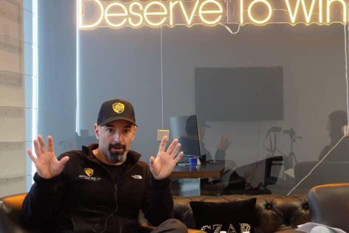 America deserves to win slogan origin, Eric J. Troutman speaking beneath a “Deserve To Win” sign at his Irvine office. youtube screenshot.