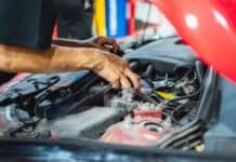 How Premium Auto Maintenance Pays Off at the Dealership Mechanic's hands working on a car engine under an open red hood. Various tools and parts are visible, conveying a sense of precision and focus.