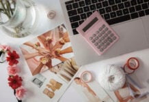Tying the Knot Without Tying Up Your Cash: Smart Ways to Finance Wedding Expenses Top-down view of a workspace with a laptop and pink calculator, surrounded by wedding planning materials including photos of bridesmaids and a bride, floral accessories, ribbon, tape, and a ball of twine, suggesting budgeting and preparation for a wedding.