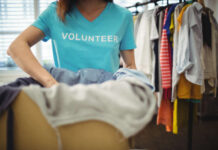Rallying the Community: How to Run a Successful Apparel Fundraiser for a Local Hero A person wearing a blue "Volunteer" shirt folds clothes. In the background, a rack with assorted colorful garments is visible, conveying community service.