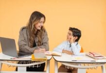 Mastering the Grade-Level Jump: Why You Need a Mentor in Your Corner A woman and a young boy sit at desks with notebooks and a laptop, smiling at each other, against a plain orange background.