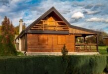 Tackling the Big Stuff: Log Cabin Projects That Require Real Planning and a Serious Supply Haul A cozy wooden cabin with closed shutters and a sloped roof sits in a lush, green landscape under a partly cloudy sky, evoking tranquility and warmth.