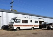 Wrapping Up the Road Trip: How to Prep Your RV for Storage A white RV with brown stripes is parked next to a metal building, with an old truck partially inside an open garage door.