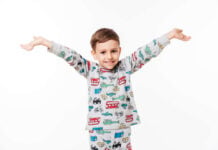 Sweet Dreams and Fresh Starts: Why You Should Buy New Pajamas for the First Day of School Young boy smiling with his arms outstretched against a white background. He's wearing pajamas featuring playful car and animal patterns, conveying joy.