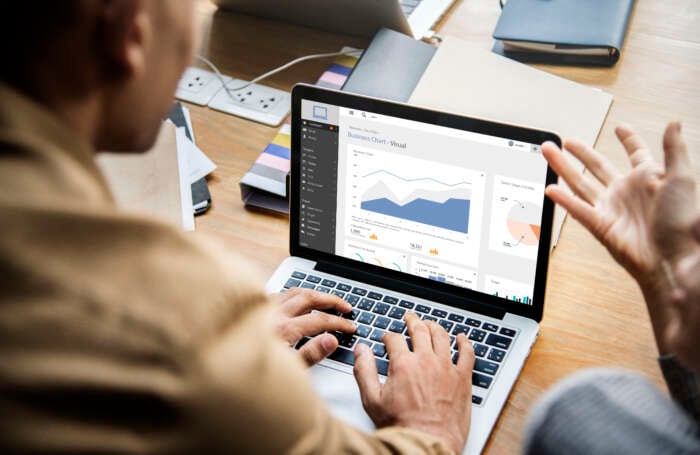 A person works at a laptop displaying an analytics dashboard with charts, gesturing as if discussing the data in a bright office setting.